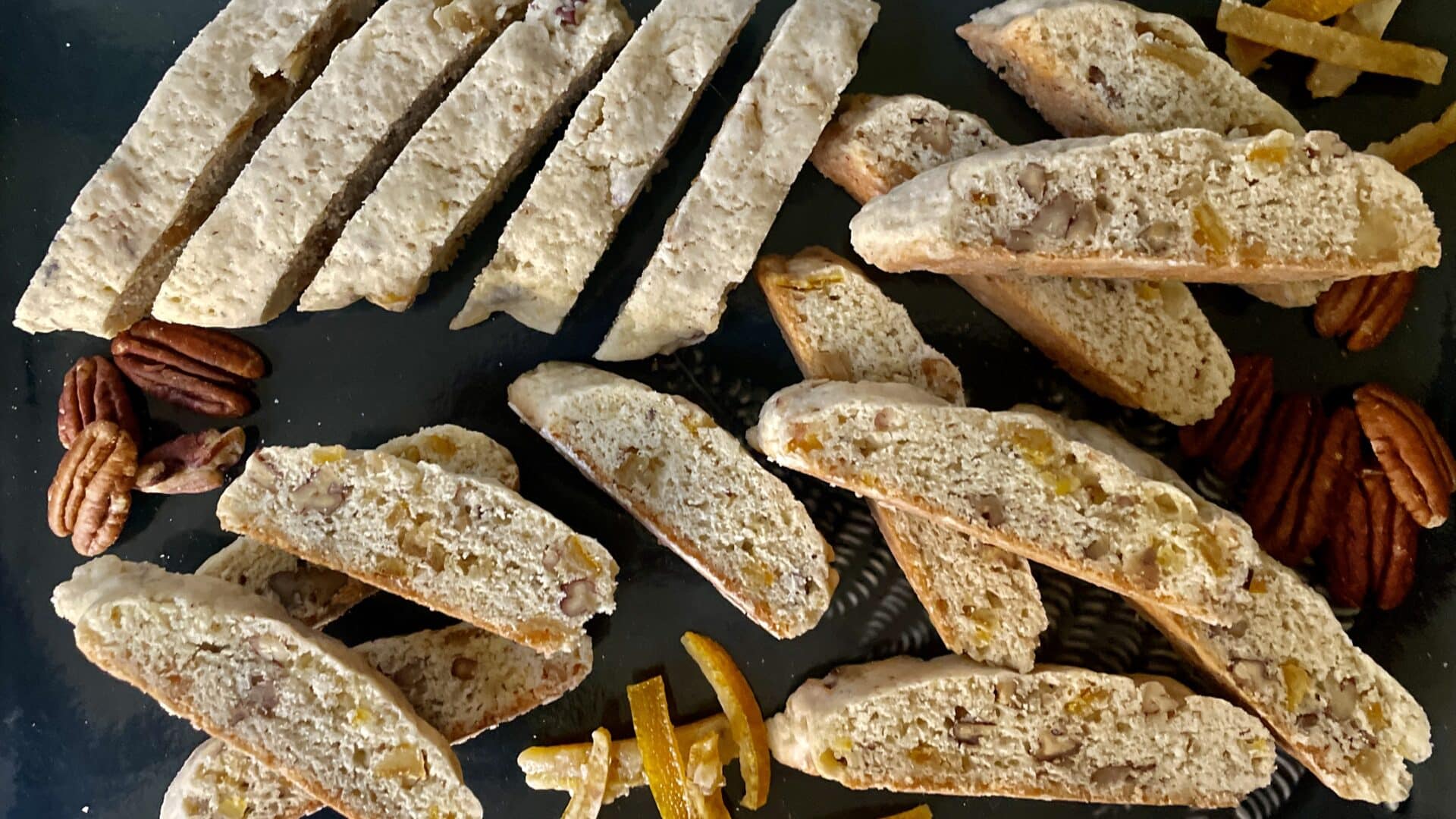 Candied Orange Peel Pecan Biscotti on a dark plate with pecans and candied orange peel