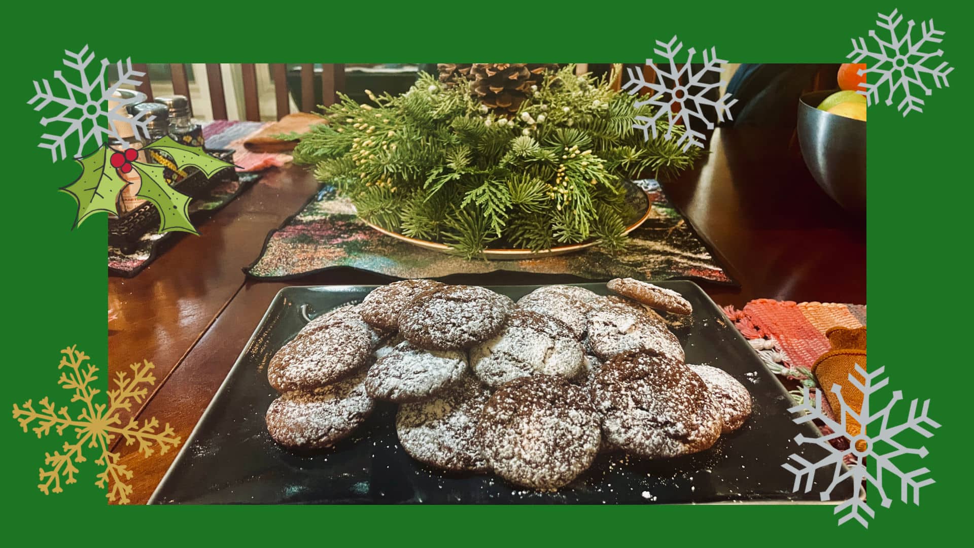 Pfeffernüsse on a dark plate surrounded by green, holly and snowflakes